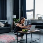 Woman using laptop while exercising at home, featuring a modern gym setting.
